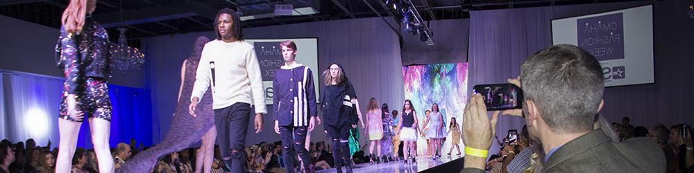 A man takes a picture of models on the runway at Omaha Fashion Week